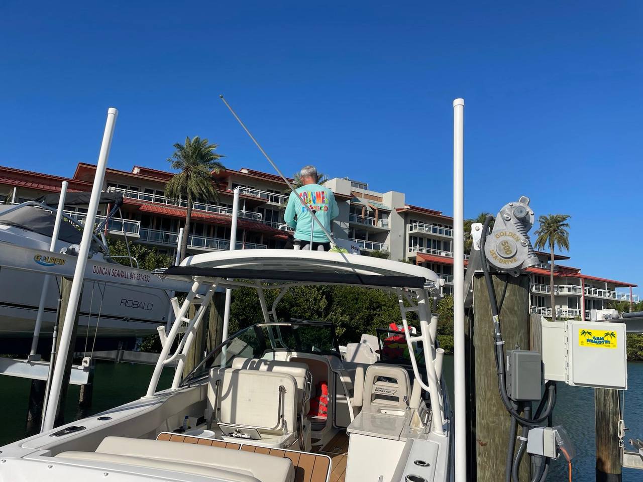Technician cleaning the top side of a boat under a clear blue sky